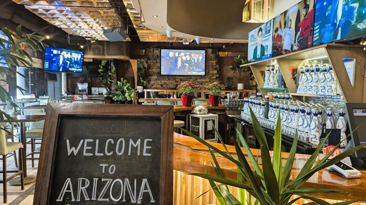 Bar area at Arizona Grill Lounge with a Welcome to Arizona chalkboard sign and TVs above the bar